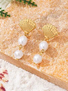 Detailed view of elegant gold shell earrings with hanging double pearls on a sand beach stone