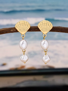 Detail of elegant gold scallop shell earrings with baroque pearls on a beach background