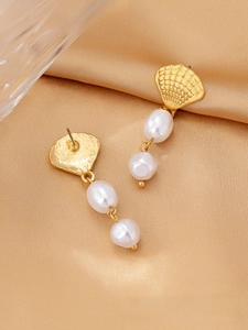 Detail of gold seashell earrings with white pearls over an elegant golden satin backdrop