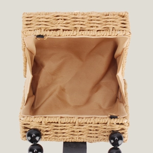 Handwoven straw bag with wooden bead handle and metal clasp in a top-down view