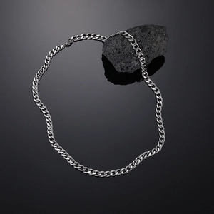 Close-up of polished silver Cuban link chain draped over black volcanic stone background