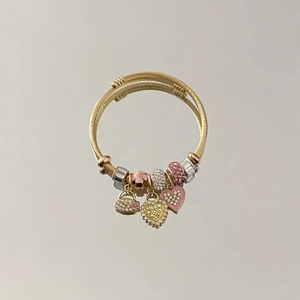 Detail of a golden twisted cuff bracelet with heart charms and pink crystal beads