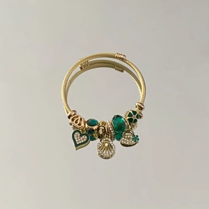 Close-up of golden wire bracelet with green beads, crystal hearts and shell charms