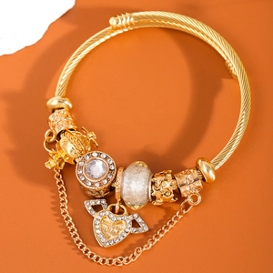 Bracciale rigido dorato con ciondoli a cuore alato e corona su uno sfondo arancione