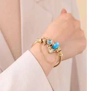 Dettaglio del bracciale dorato con ciondoli a cuore blu e corona sul polso