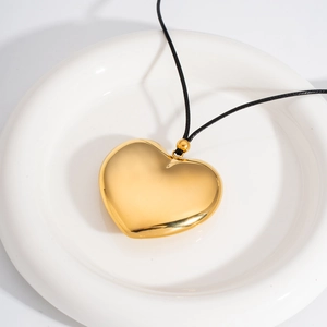 Polished hollow heart pendant on black cord necklace shown in a ceramic tray
