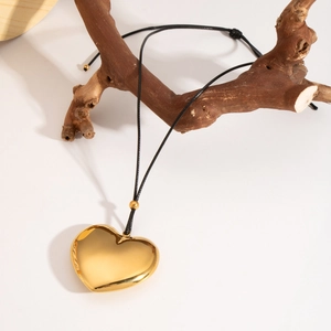 Macro view of 18K gold hollow heart pendant on black cord hanging from a tree branch