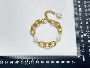 Dettaglio di un bracciale a catena dorata con perle barocche bianche e scala di misurazione