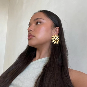 Close-up of a model wearing large 18K gold plated flower earrings with a center pearl