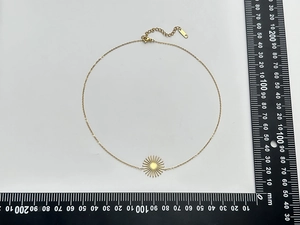 Mise à plat d'un collier pendentif soleil doré avec échelle de mesure sur fond blanc