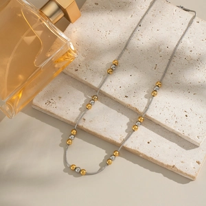 Primo piano della collana di perle bicolore oro e argento su sfondo di pietra travertino