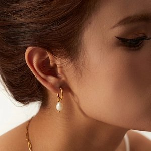 Detail of a natural freshwater pearl earring with a gold hoop on a model's ear