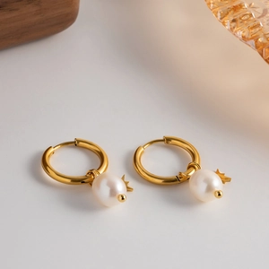 Detail of gold star charm hoop earrings with natural freshwater pearls on a warm surface