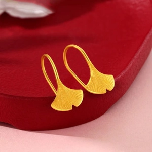 Detailed macro view of golden ginkgo leaf earrings with realistic vein texture on red stand