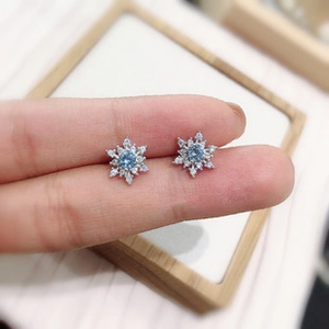 Detailed close-up of snowflake stud earrings with blue center stone and silver plating