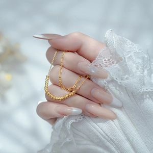Close-up of golden beaded chain necklace held by model with white lace background