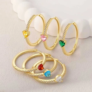 Detalle de pendientes de aro dorados con piedras de corazón de colores y circonitas