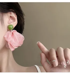 Detail shot of oversized pink petal earrings with green beads on a female model