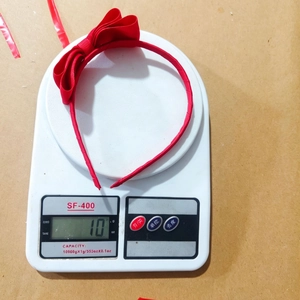 Detailed view of red grosgrain bow headband weighing 10g on a digital scale