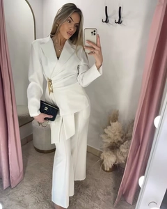 Detail of white wrap blazer with gold metal buckle and matching high-waisted trousers