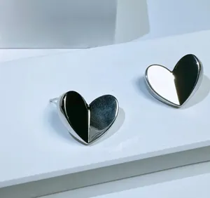 Detailed close-up of 3D geometric silver heart stud earrings with faceted metal design