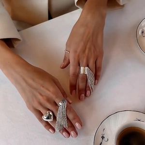 Detail of silver tassel rings with heart charm shown in a lifestyle hand-worn setting