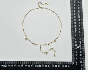 Close-up detail of a minimalist gold Y-necklace with beads shown on a measuring scale