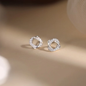 Macro shot of silver knot stud earrings with micro-pave crystals on a warm background