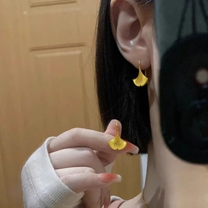 On-ear view showing the scale of gold ginkgo leaf dangle earrings with matte texture