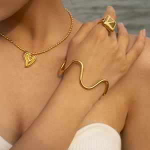 Close-up of gold wavy open bangle and heart pendant necklace on a female model