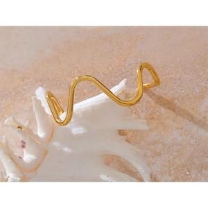 Macro detail of gold wavy minimalist cuff bracelet on white seashell with soft lighting