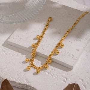 Detail of 18K gold-plated titanium steel bracelet with ball pendants on a stone surface