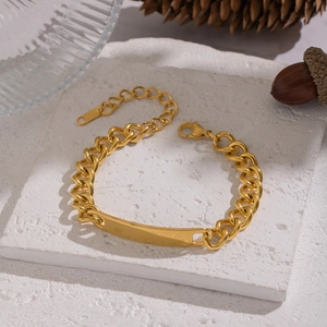 Détail macro d'un bracelet gourmette doré disposé sur un plateau en pierre blanc