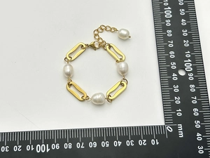Détail d'un bracelet en perles baroques avec maillons dorés et règle de mesure sur fond blanc