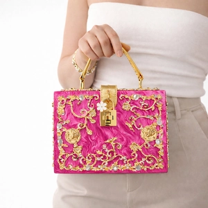 Detailed view of pink acrylic evening bag with hollow gold metal floral carving
