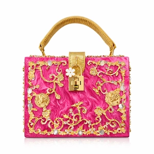 Macro view of bright pink acrylic clutch featuring intricate gold floral carving and crystals