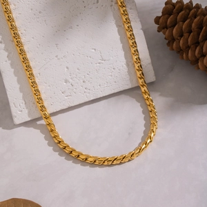 Dettaglio di una collana a catena cubana dorata su pietra bianca con decoro naturale