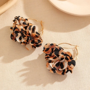 Dettaglio di orecchini a cerchio dorati con fiori in tessuto leopardato 3D su panno beige