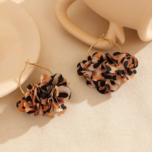 Dettaglio degli orecchini a cerchio con fiori in tessuto leopardato su panno beige