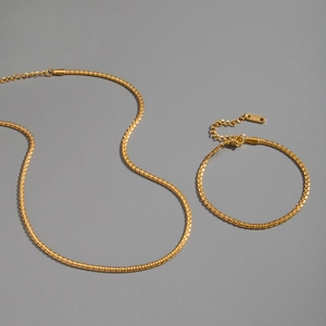 Detail of gold box chain necklace and bracelet set with lobster clasp on grey background