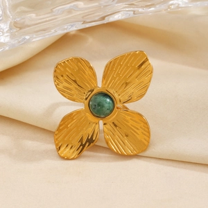 Gold textured flower ring with green natural stone inlay on soft fabric background