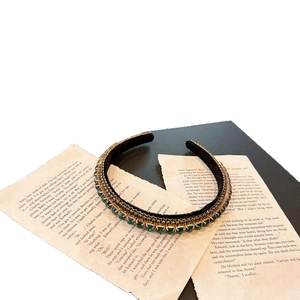 Luxurious emerald green rhinestone headband with gold setting on black velvet base
