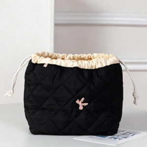Detail of black quilted drawstring makeup bag with pink embroidered letter K detail