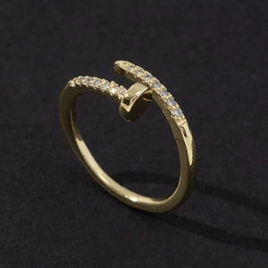 Top view of gold nail-shaped ring with white zircons on black matte background