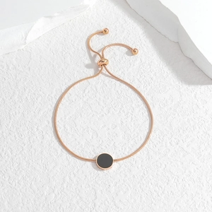 Rose gold adjustable snake chain bracelet with black circular charm on white stone