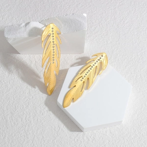 Polished gold feather drop earrings with crystal rhinestones on a white geometric stage