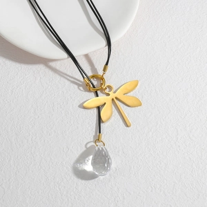 Golden dragonfly necklace with crystal droplet pendant on a black cord over white surface