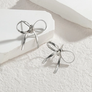 Minimalist silver bow earrings with metal snake chain texture on white stone background