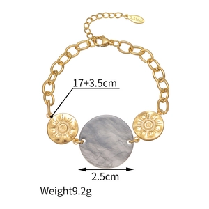 Detail of gold stainless steel bracelet with sunburst discs and grey resin pendant