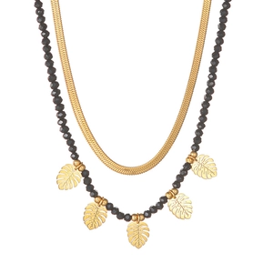 Double-layer cross necklace with black beads and gold monstera leaf charms on white surface